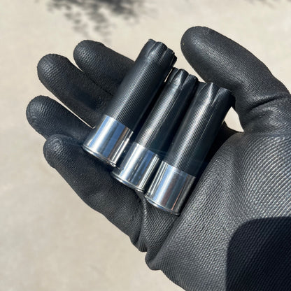 Three black shotgun shells with high brass bottoms held in a black gloved hand