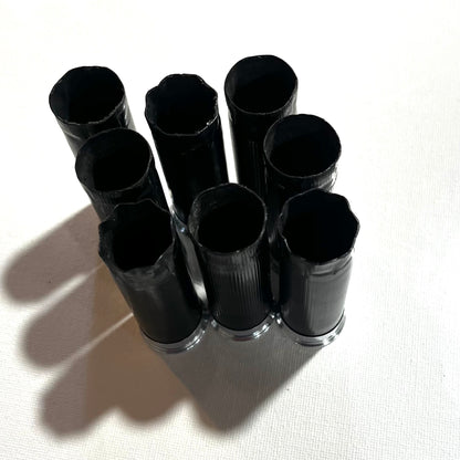 8 black shotgun shell hulls with silver bases viewed from above, open crimped ends visible in cluster