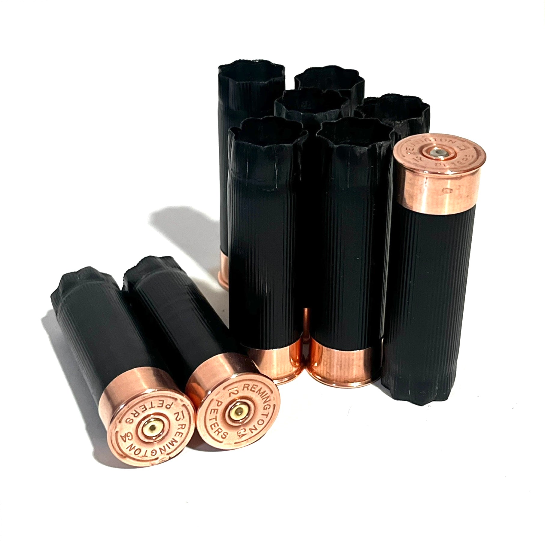 8 black shotgun shell hulls with copper bases standing and laid on white background, Remington Peters headstamps visible
