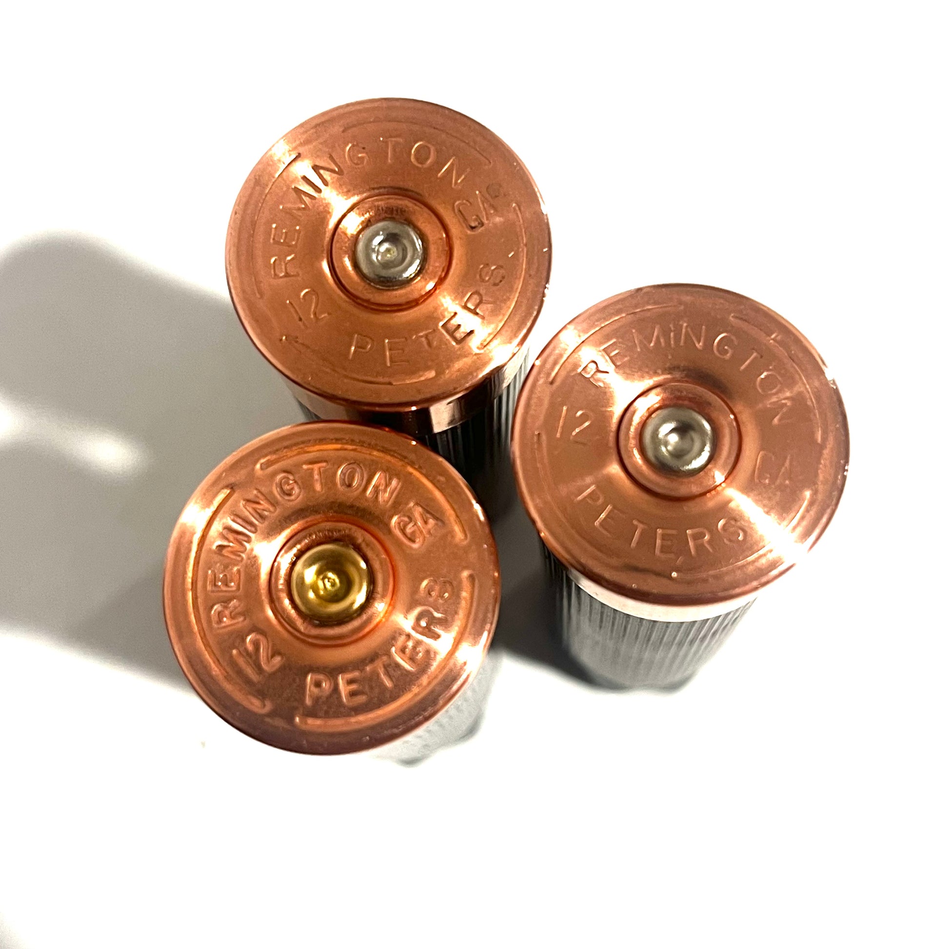 3 black shotgun shell hulls viewed from below showing copper Remington Peters 12 gauge headstamps on white background