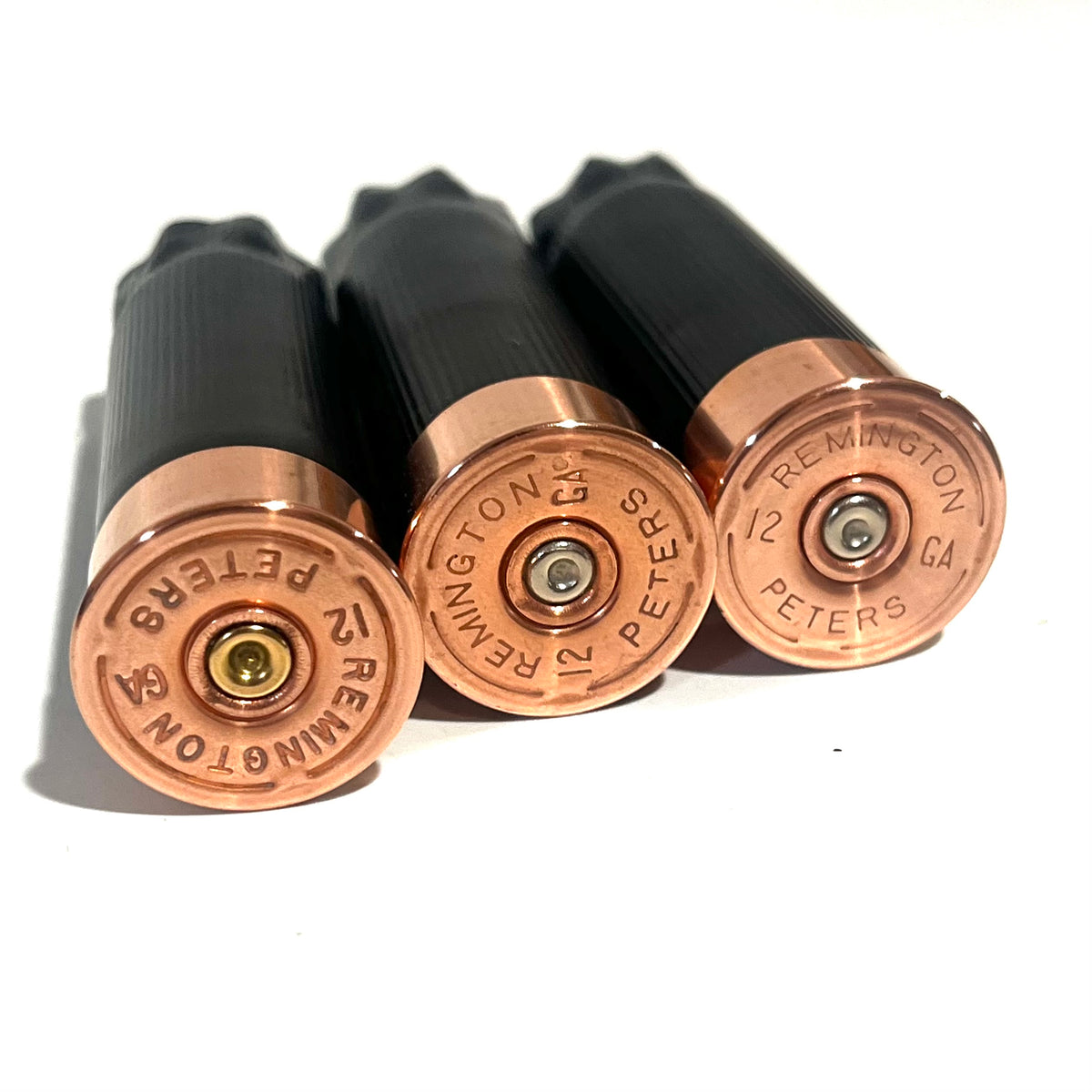 3 black shotgun shell hulls with copper bases stacked diagonally on white background