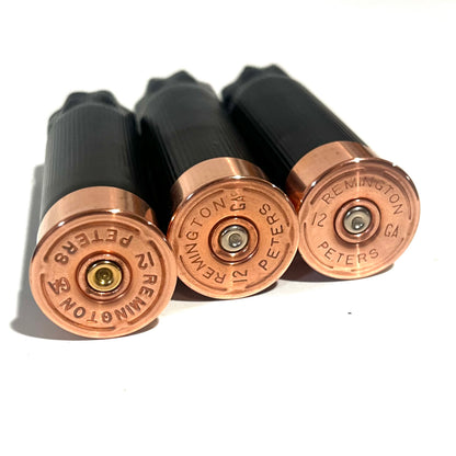 3 black shotgun shell hulls with copper bases stacked diagonally on white background