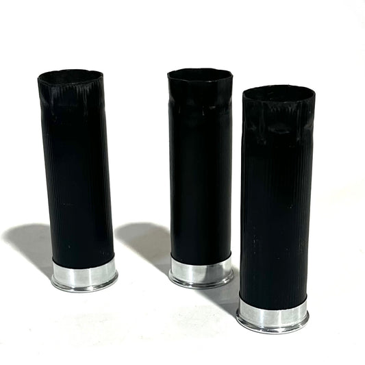 3 black shotgun shell hulls standing upright with silver bases on white background