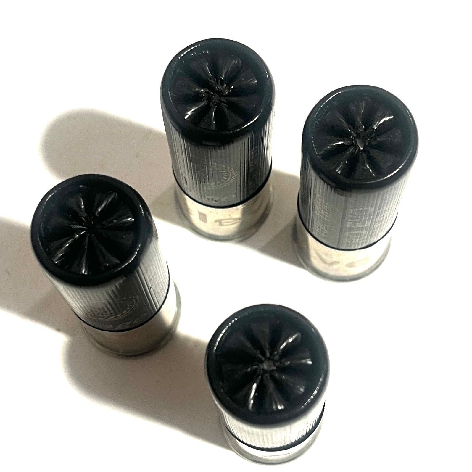 Four black 12-gauge shotshells viewed from above, showing star-crimped tops and silver metal bases.