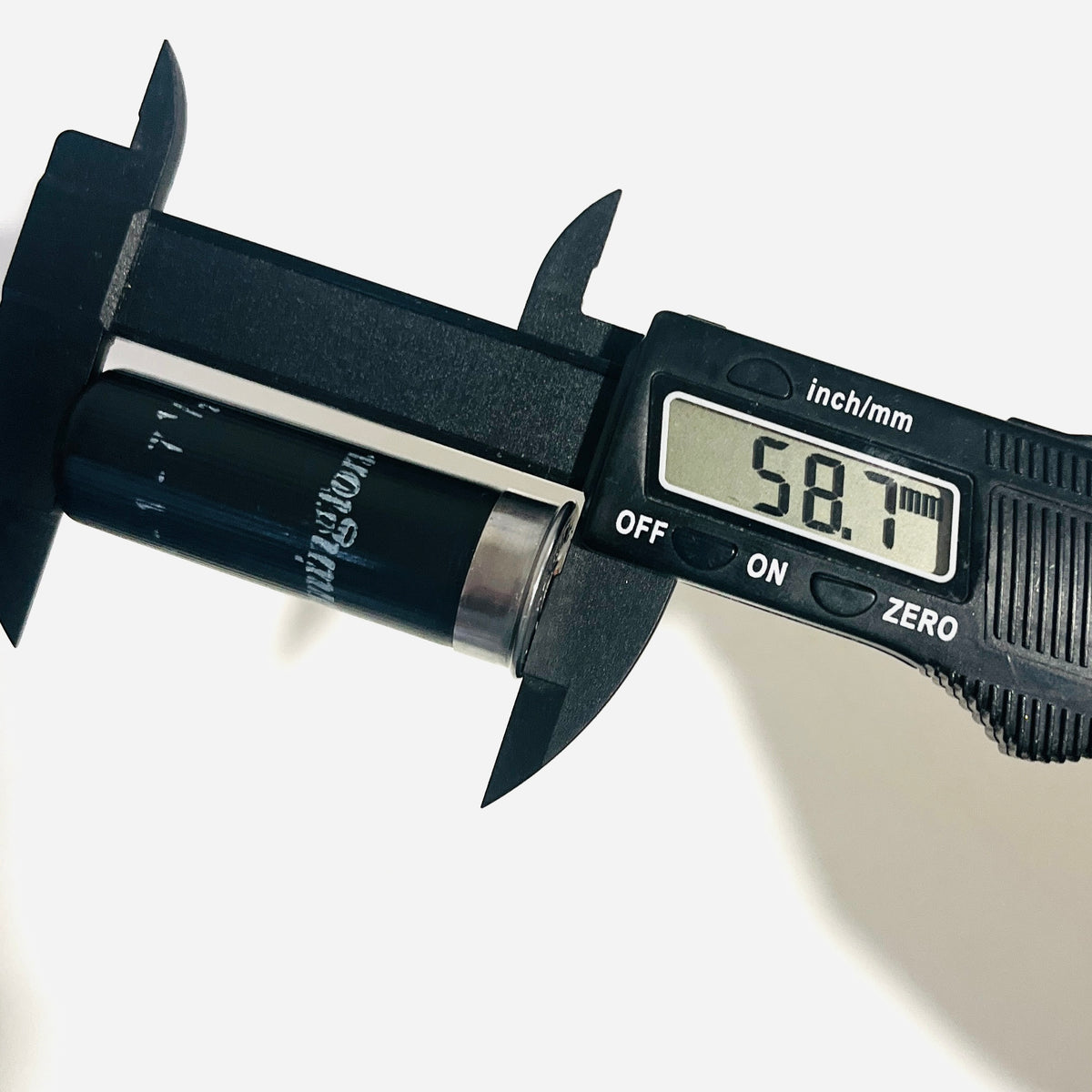 Digital caliper reading 58.7 mm along the crimped length of a once-fired black Remington dummy shell