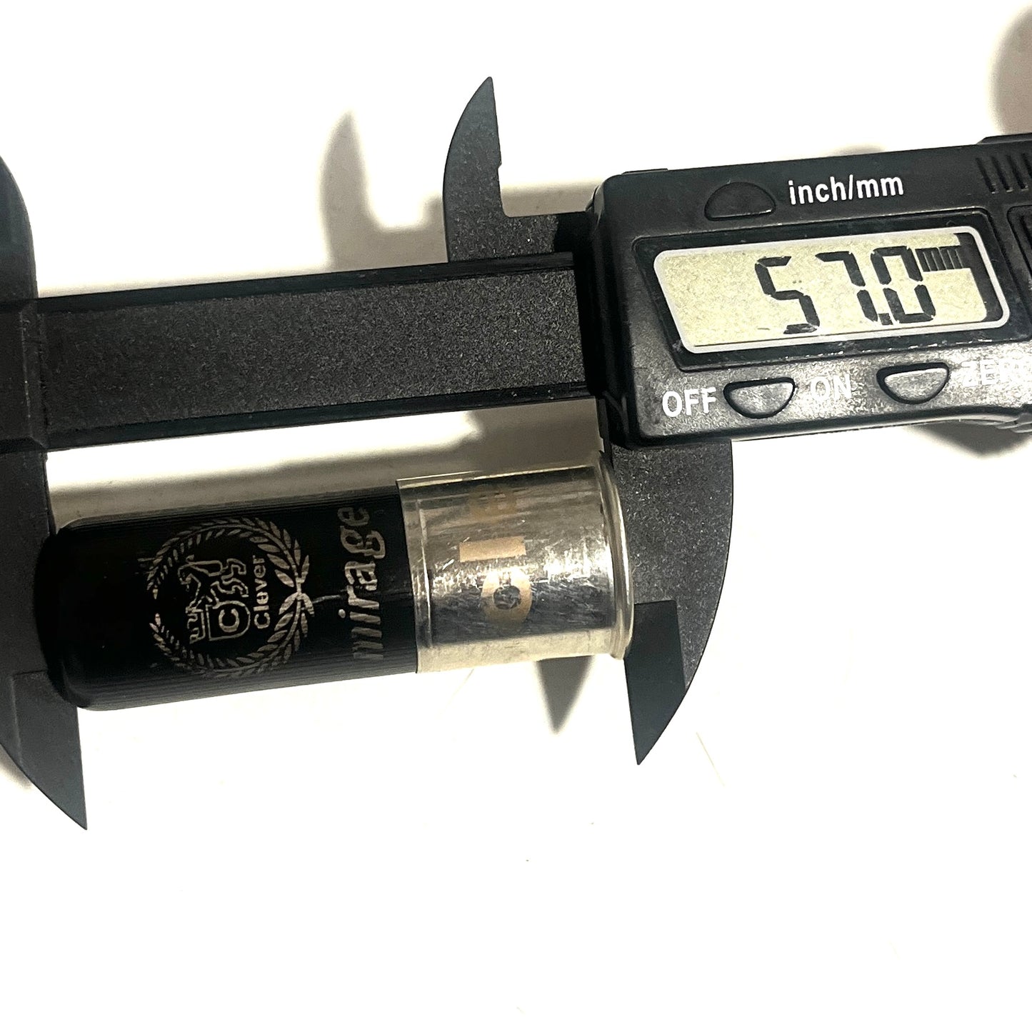 Digital caliper measuring the overall length of a black 12-gauge hull with "mirage" branding, reading 57.0 mm.