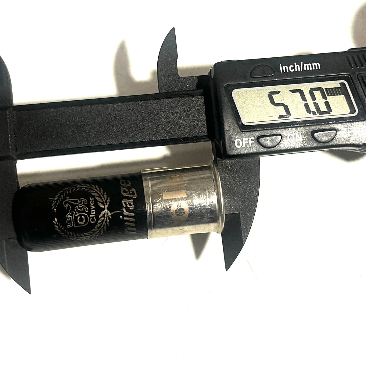 Digital caliper measuring the overall length of a black 12-gauge hull with "mirage" branding, reading 57.0 mm.