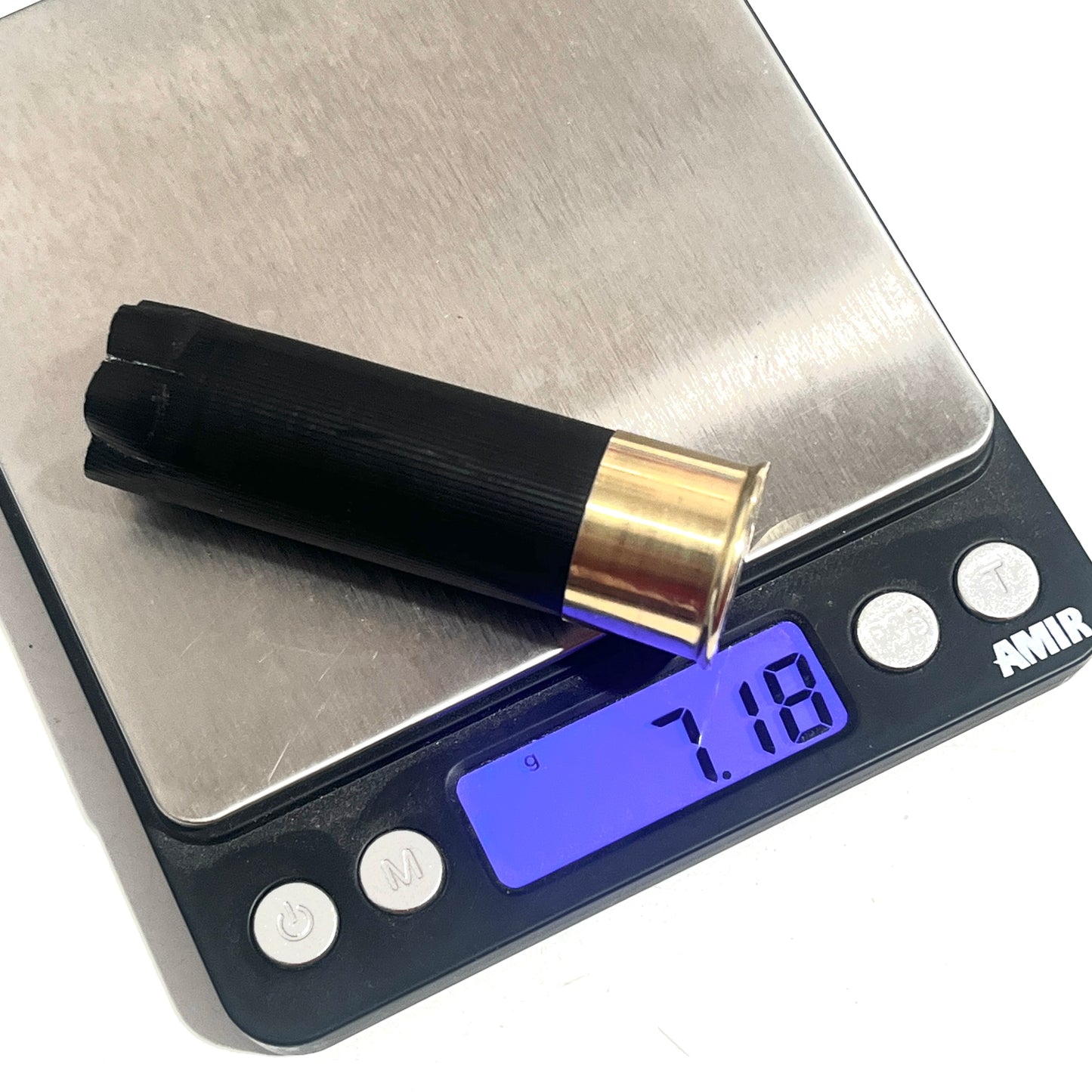 A once-fired black shotgun hull no writing  lying diagonally on a digital scale reading 7.18 grams