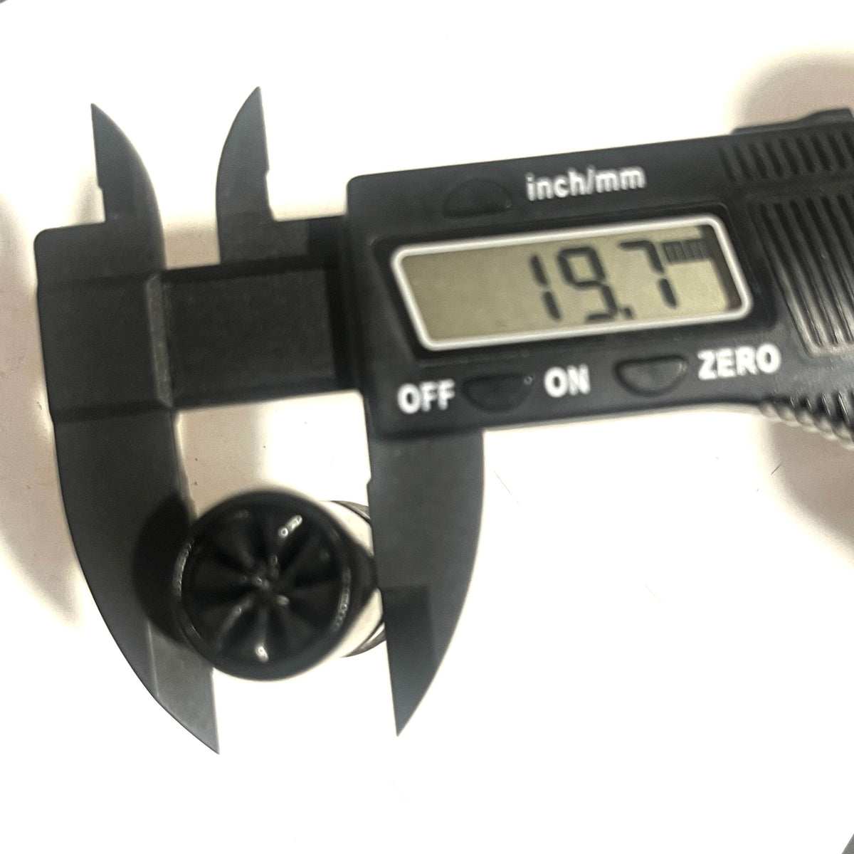Digital caliper measuring the star-crimped top of a black 12-gauge dummy round, reading 19.7 mm.