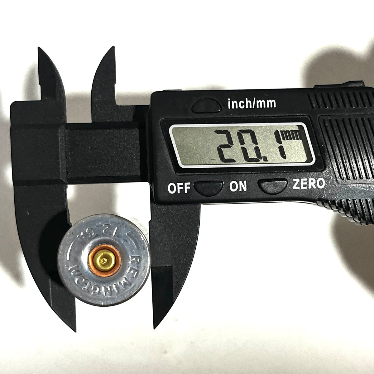 Digital caliper reading 20.1 mm across the hull diameter of a spent black Remington dummy shell, headstamp facing up