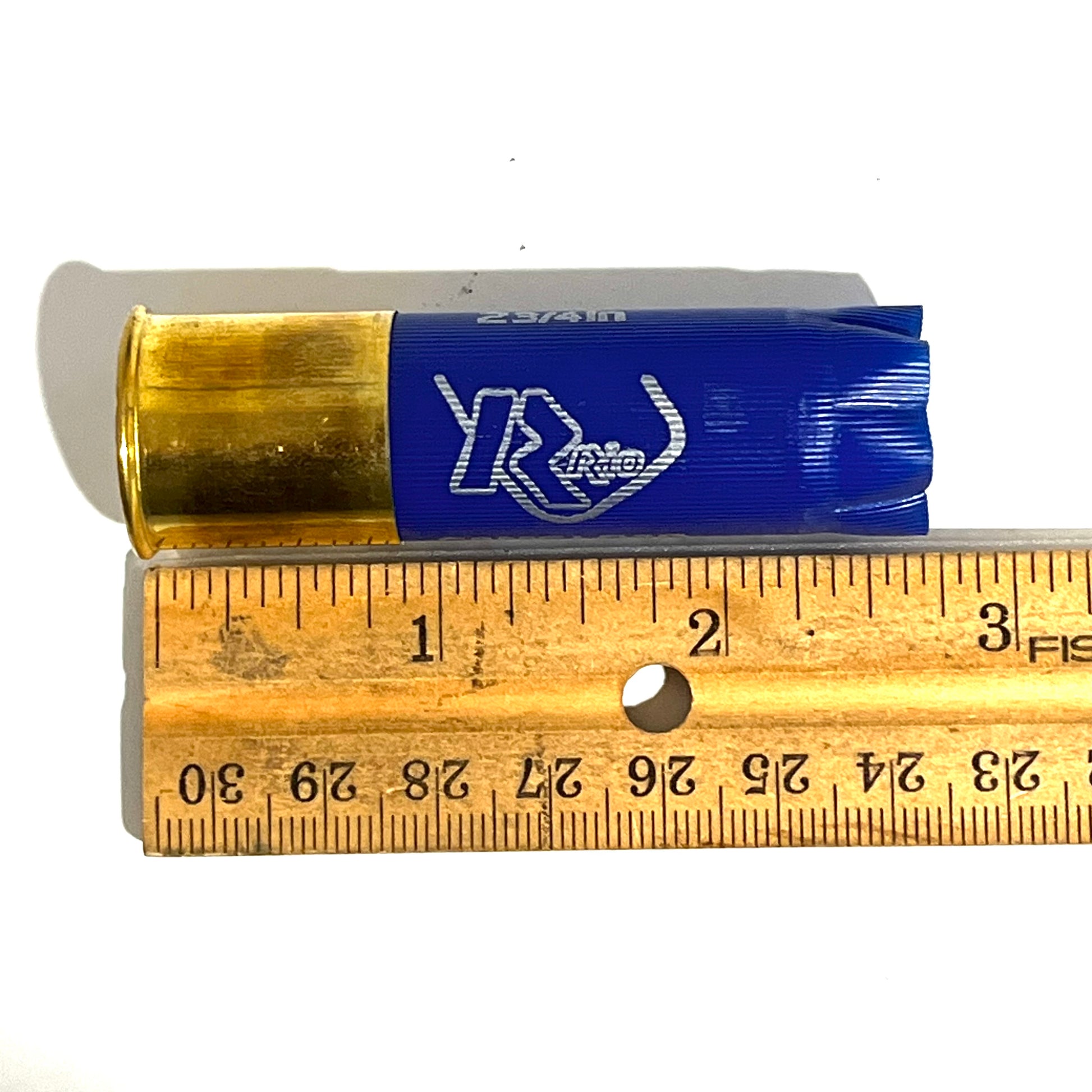 Single empty blue 12 gauge RIO shotgun shell with brass base next to a wooden ruler showing approximately 2.75 inches in length