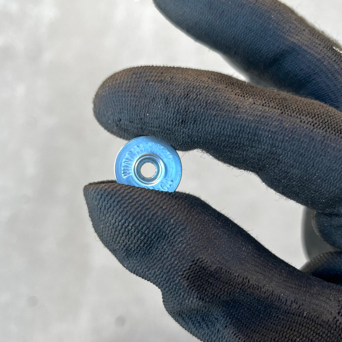 Blue-painted Winchester 20 GA shotgun shell slice held between gloved fingers