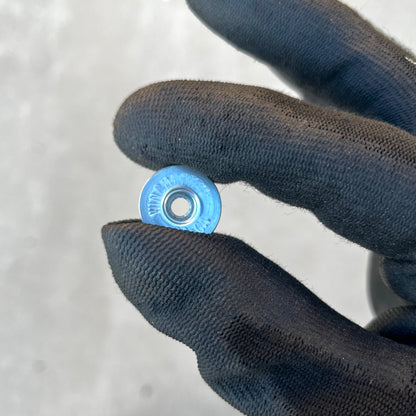 Blue-painted Winchester 20 GA shotgun shell slice held between gloved fingers