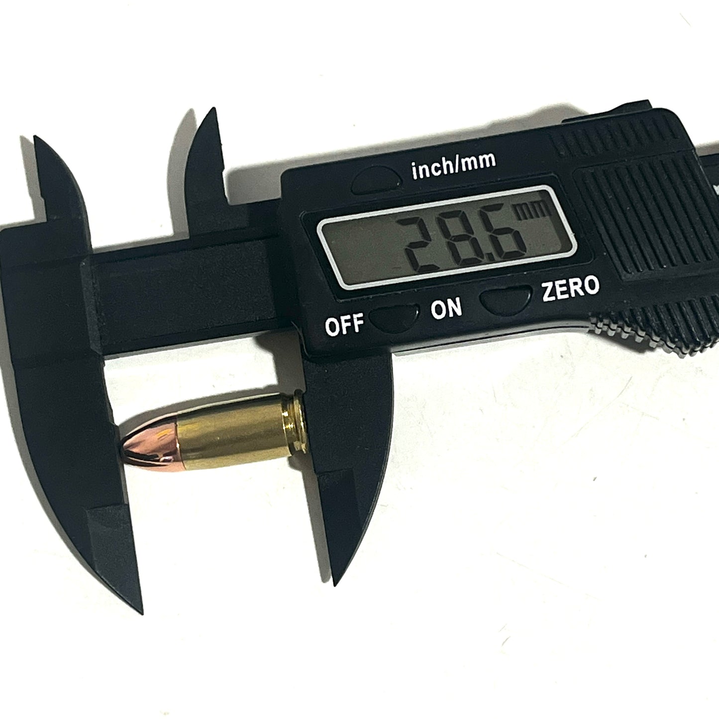 Black digital caliper measuring the total length of a brass 9mm dummy round, showing a display reading of 28.6 mm.