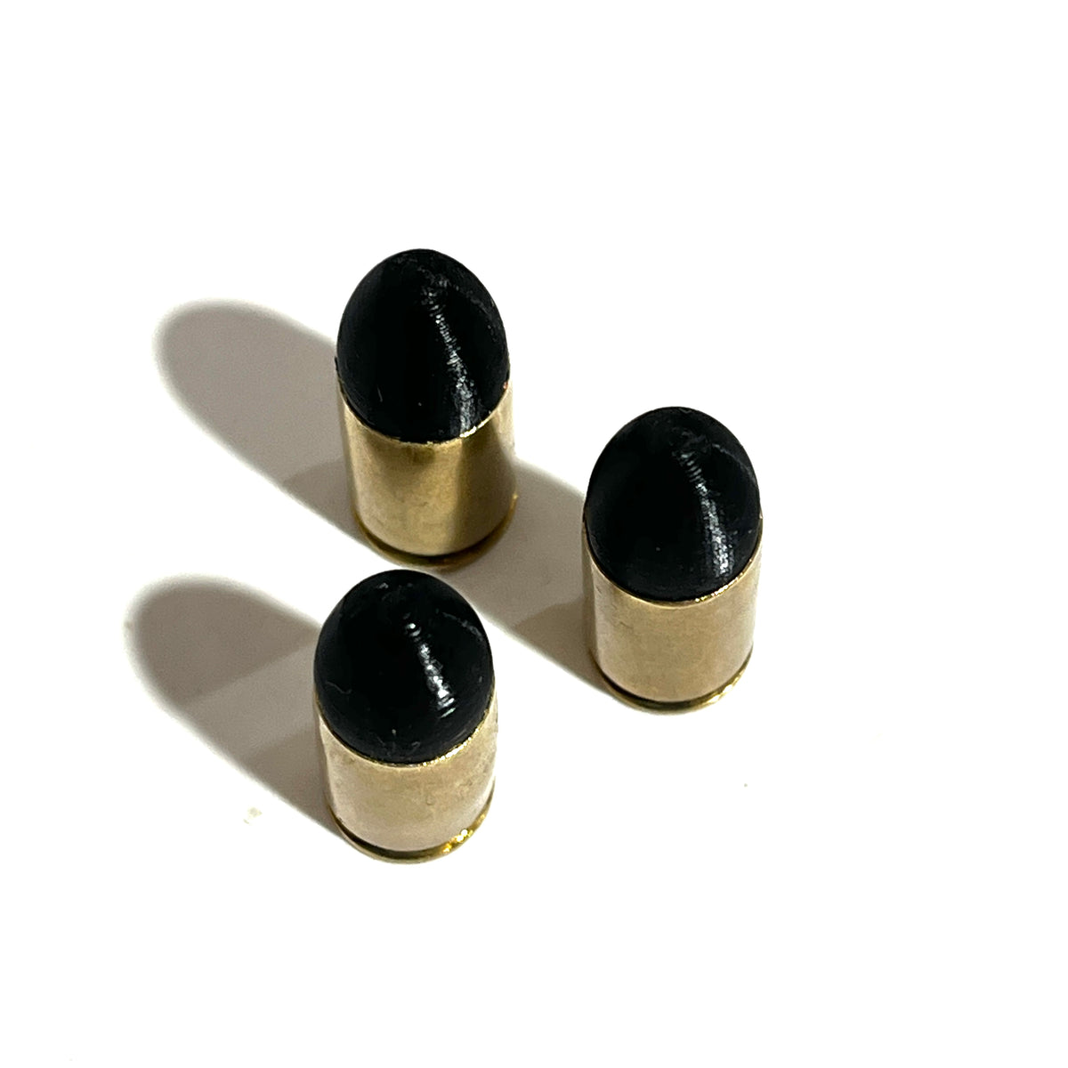 3 fake 9mm Luger dummy rounds with black painted tips standing on white background