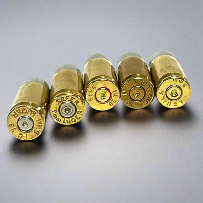 Five brass 9mm Luger cartridges lined up base-first, showing assorted headstamp markings and spent primers.
