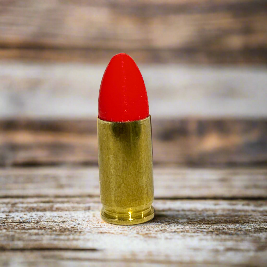 Single fake 9mm Luger dummy round with red painted tip standing on weathered wood plank background