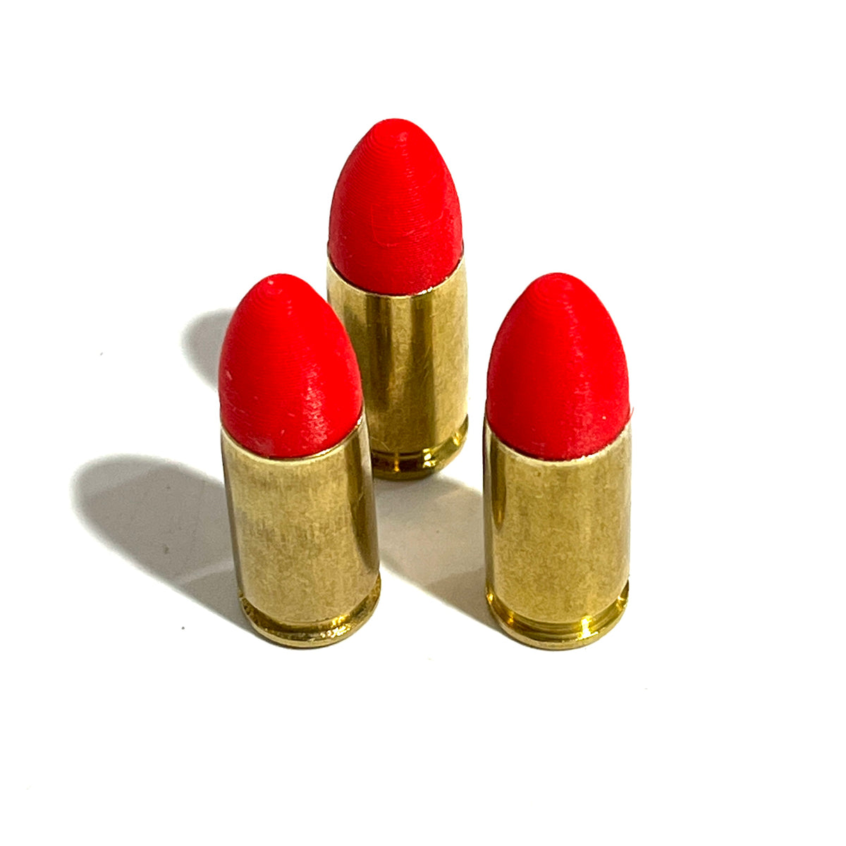 3 fake 9mm Luger dummy rounds with red painted tips standing in staggered row on white background