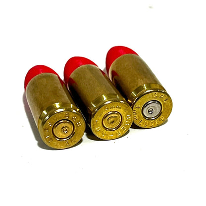 3 fake 9mm Luger dummy rounds with red painted tips viewed from brass base, mixed headstamp markings visible