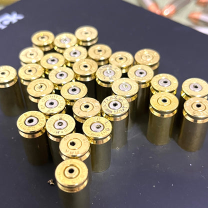 Rows of polished brass 9mm empty casings with drilled headstamps arranged on a dark tabletop