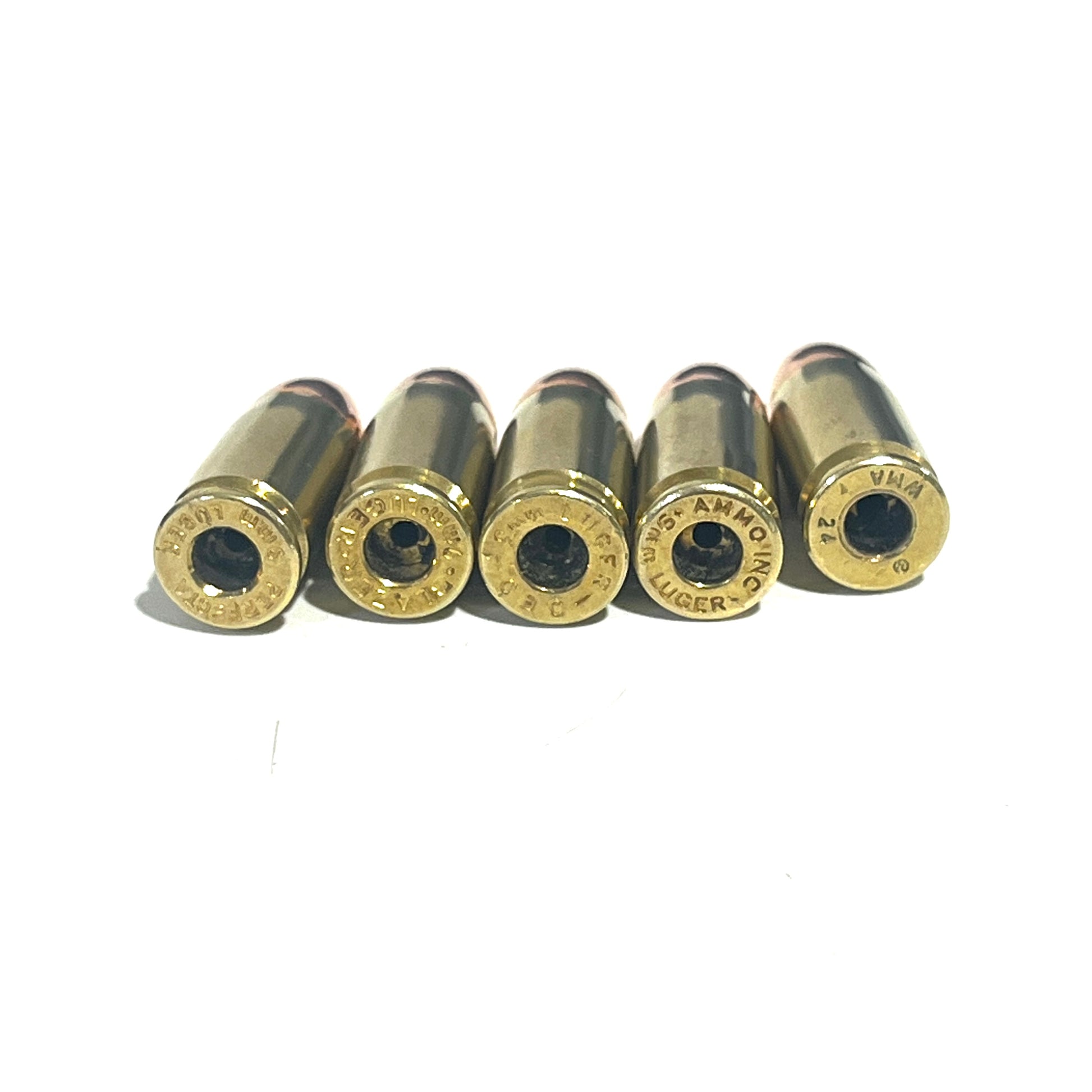 Five deprimed 9mm brass casing bases with empty primer pockets lined up in a row on a white background.