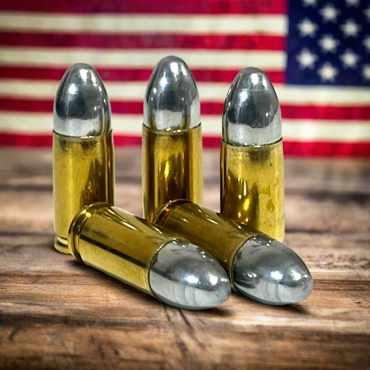 Five brass 9mm dummy cartridges on a wood surface in front of an American flag.