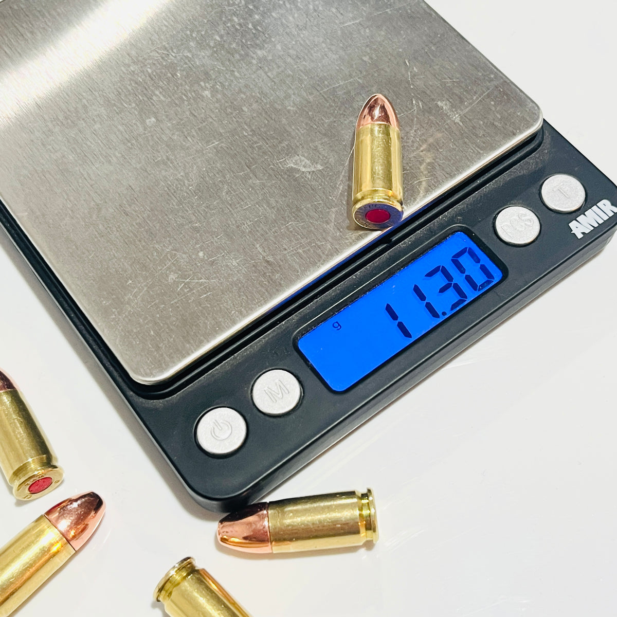 One once-fired brass cartridge on a digital scale reading 11.30 g, with more copper-tipped rounds nearby