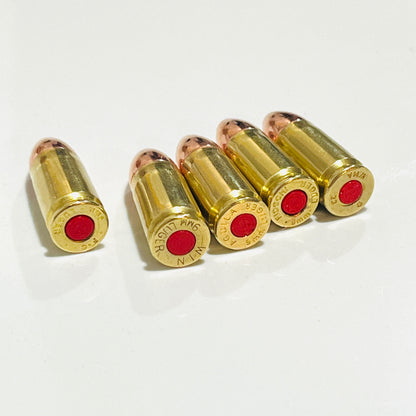 Four once-fired brass snap caps grouped beside a fifth set apart, bases angled to show red primers and headstamps