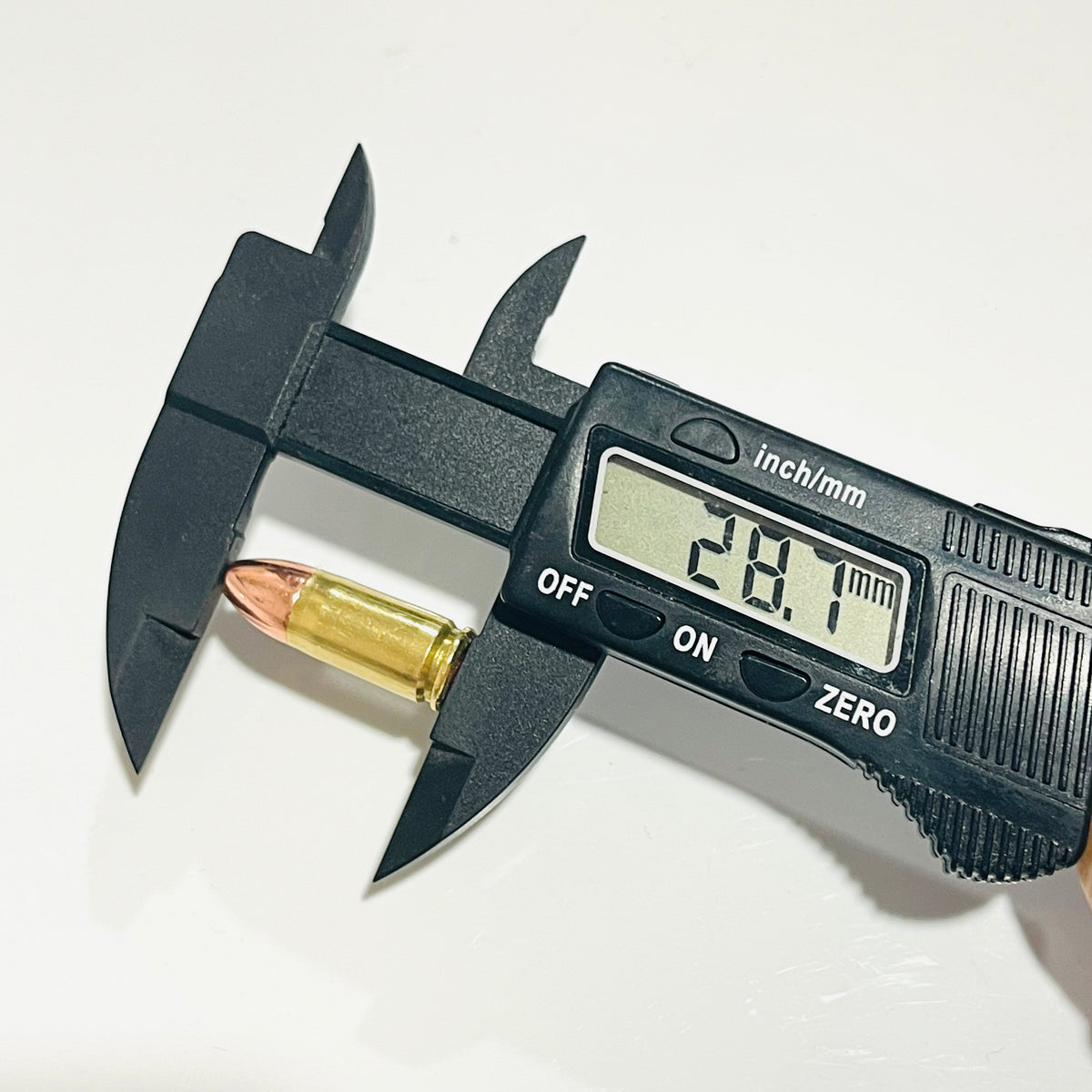Digital caliper reading 28.7 mm across the overall length of one used brass dummy round with a copper round-nose tip