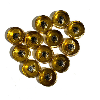 Twelve polished brass 12 gauge shotgun shell bottoms viewed from the underside showing drilled centers