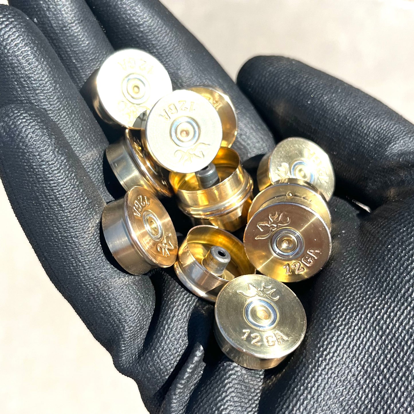 A handful of polished brass 12 gauge shotgun shell bottoms with Browning headstamps held in a black gloved hand