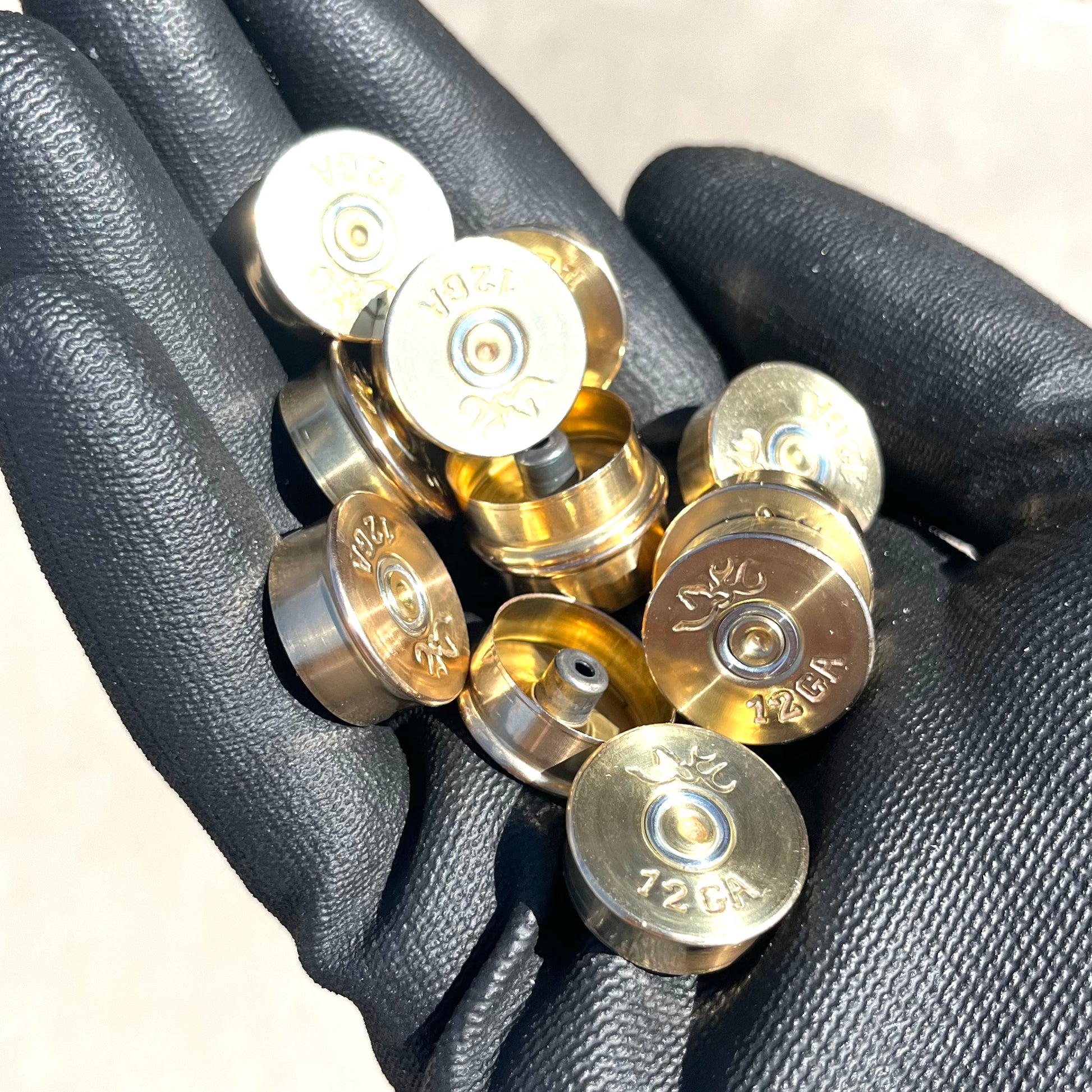 A handful of polished brass 12 gauge shotgun shell bottoms with Browning headstamps held in a black gloved hand