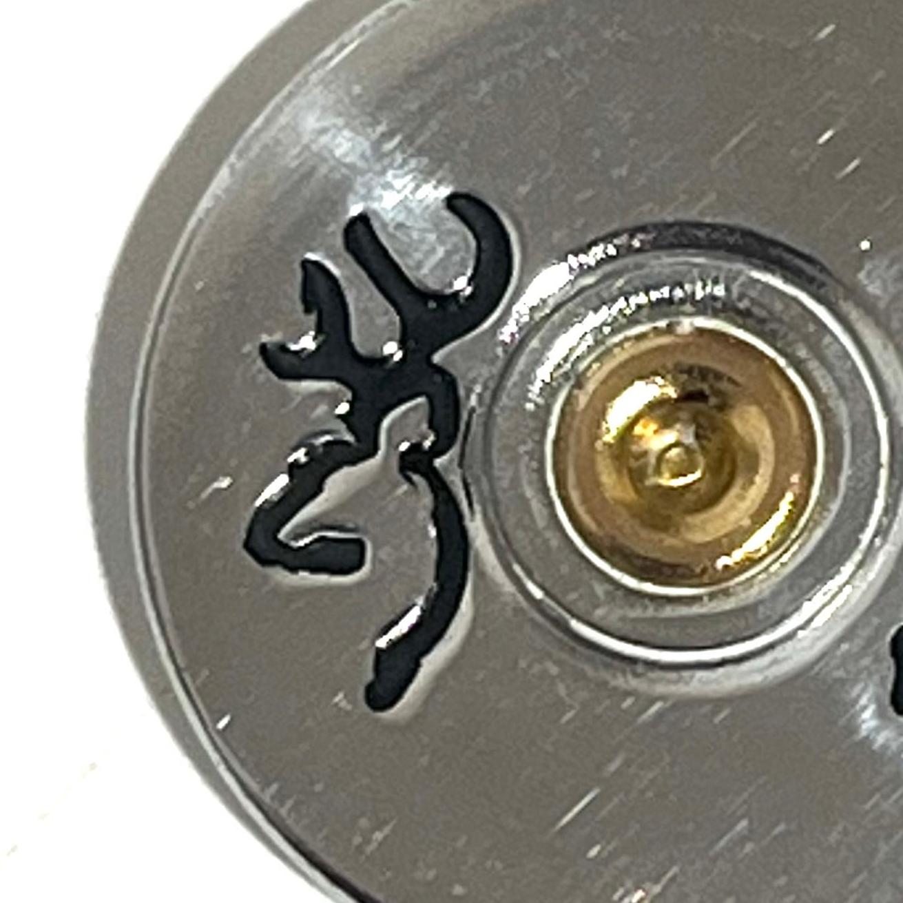Close-up of the black Browning Buckmark beside the brass-colored center of a silver shell slice