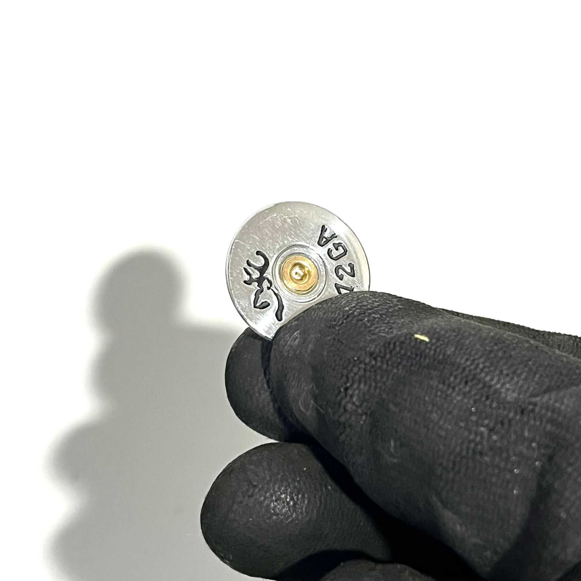 Small silver Browning shotgun shell slice held between black-gloved fingers