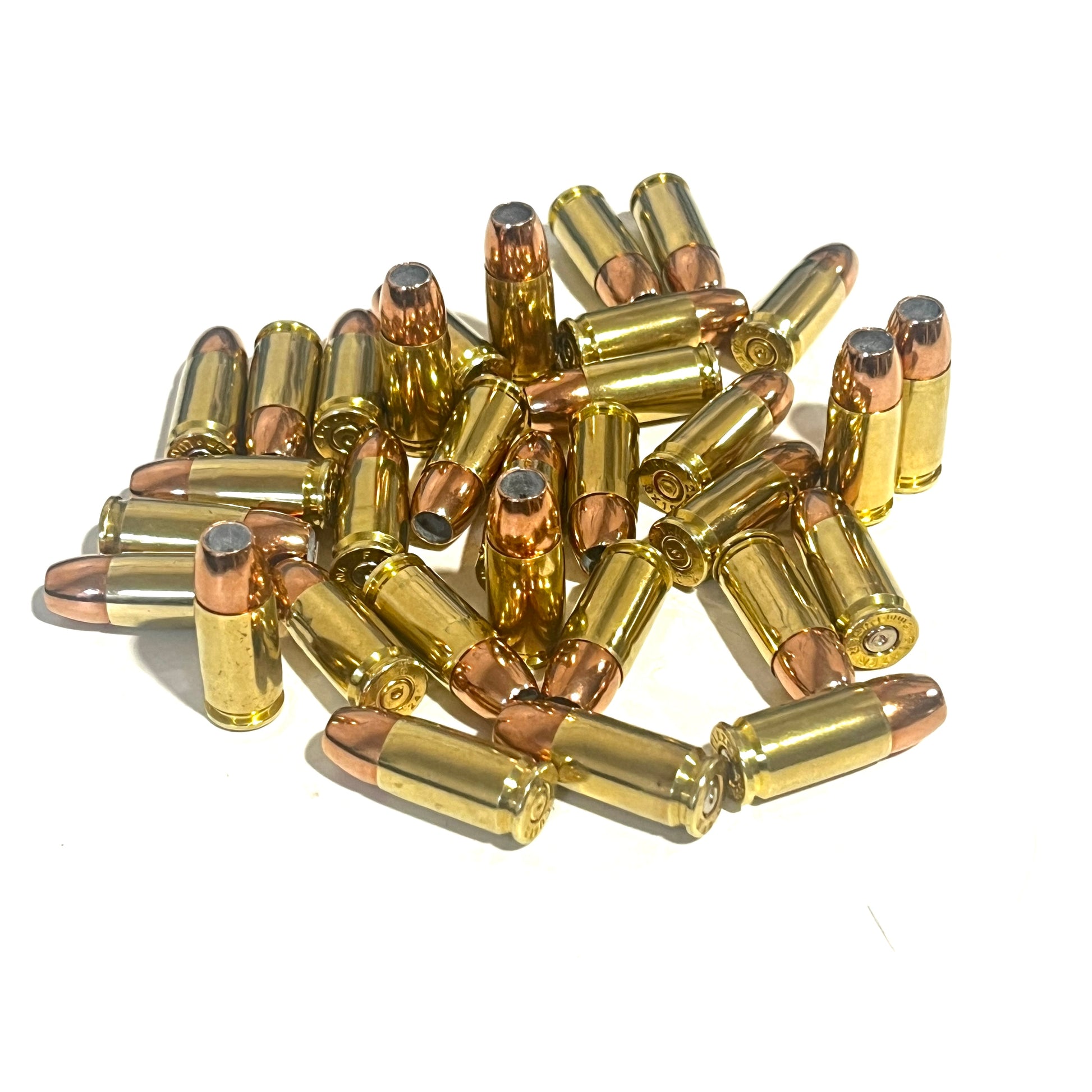 Unsorted heap of brass 9mm dummy cartridges with jacketed hollow point copper bullets on a white background.