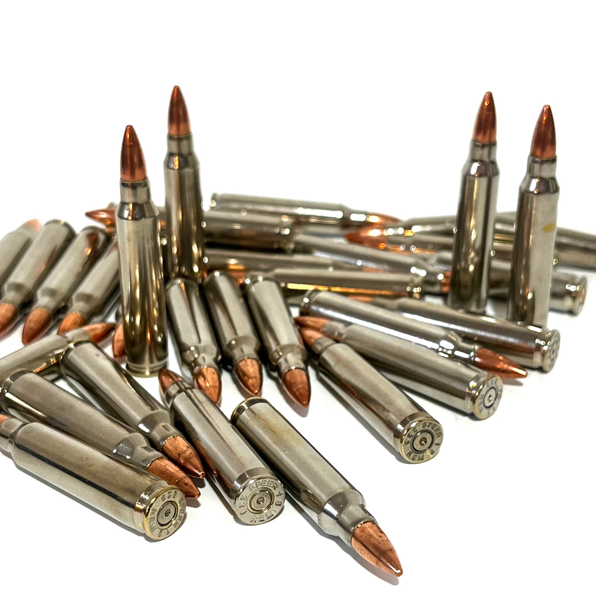 Large pile of nickel .223 dummy rifle cartridges with copper bullet tips displaying stamped base headstamps.