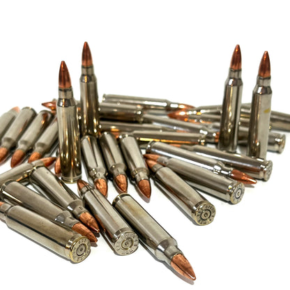 Large pile of nickel .223 dummy rifle cartridges with copper bullet tips displaying stamped base headstamps.