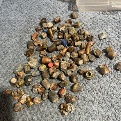 Pile of deformed spent bullet fragments on a gray towel next to a plastic ammo case
