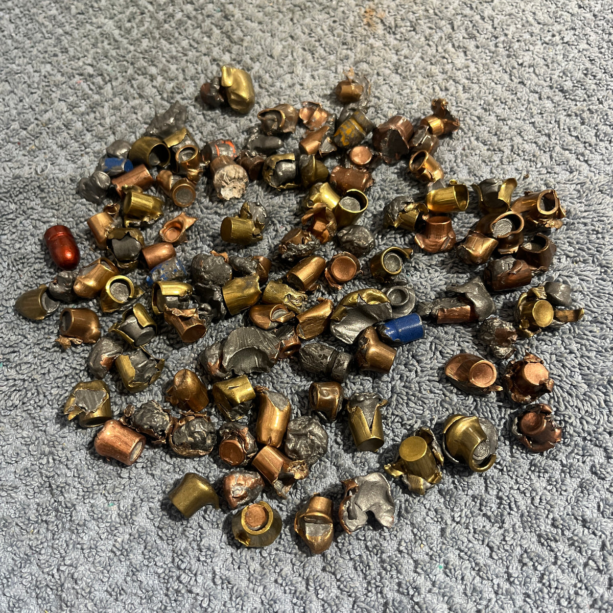 Pile of deformed spent bullet fragments on a gray towel next to a blue tarp