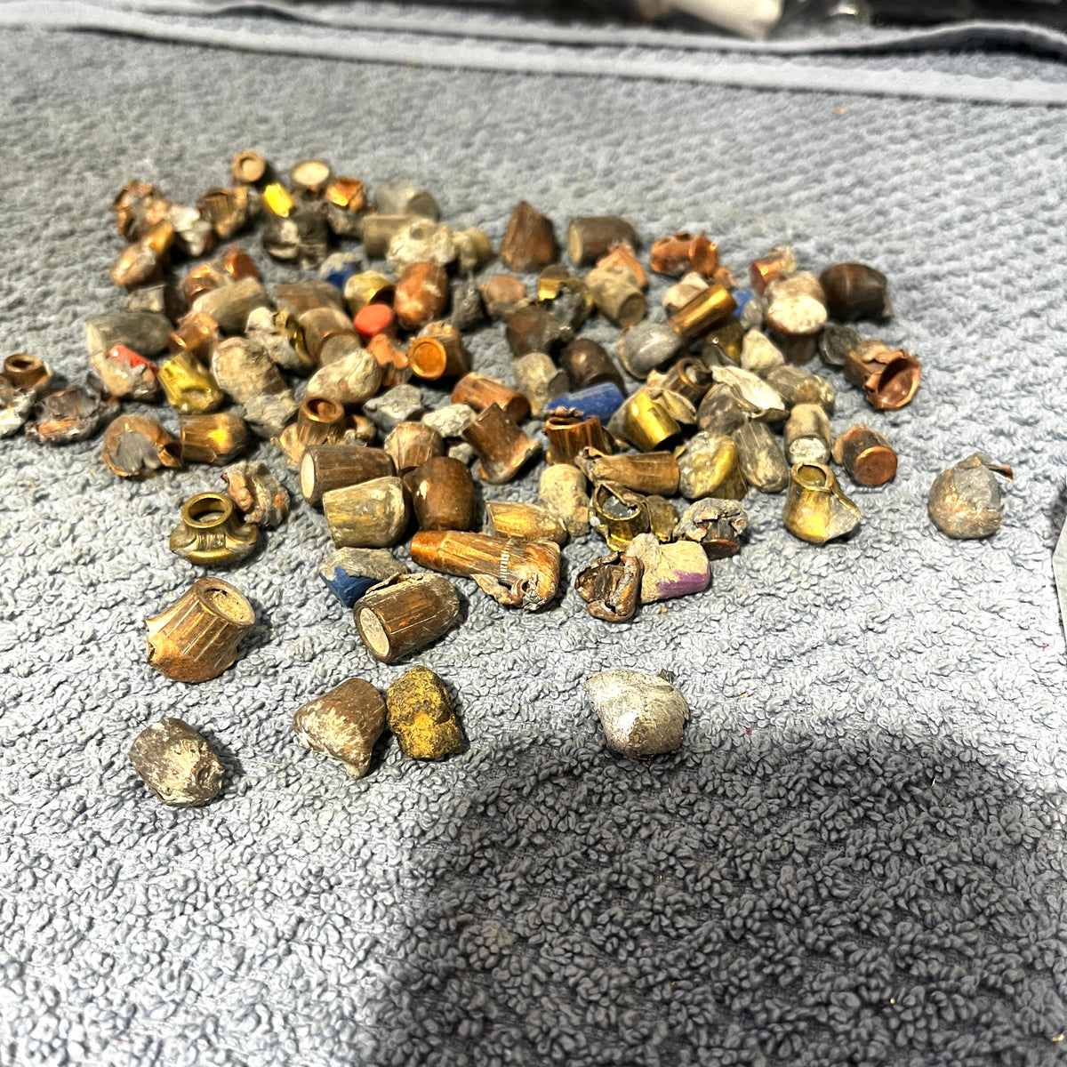 Pile of deformed copper and brass spent bullet fragments on a gray towel