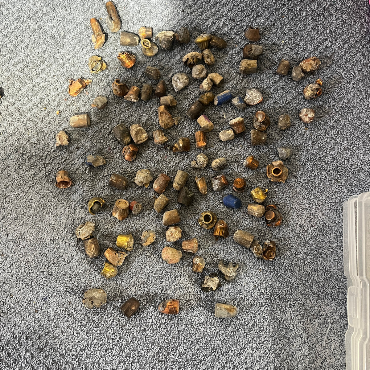 Pile of deformed spent bullet fragments on a gray towel next to a plastic storage box
