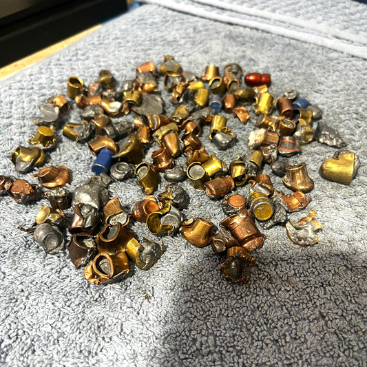Pile of deformed copper and brass spent bullet fragments in various shapes, on a gray towel