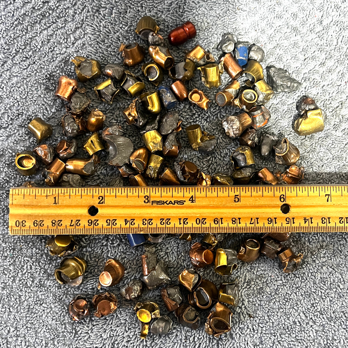 Pile of deformed spent bullet fragments measured next to a ruler on a gray towel