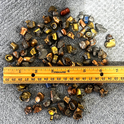 Pile of deformed spent bullet fragments measured next to a ruler on a gray towel