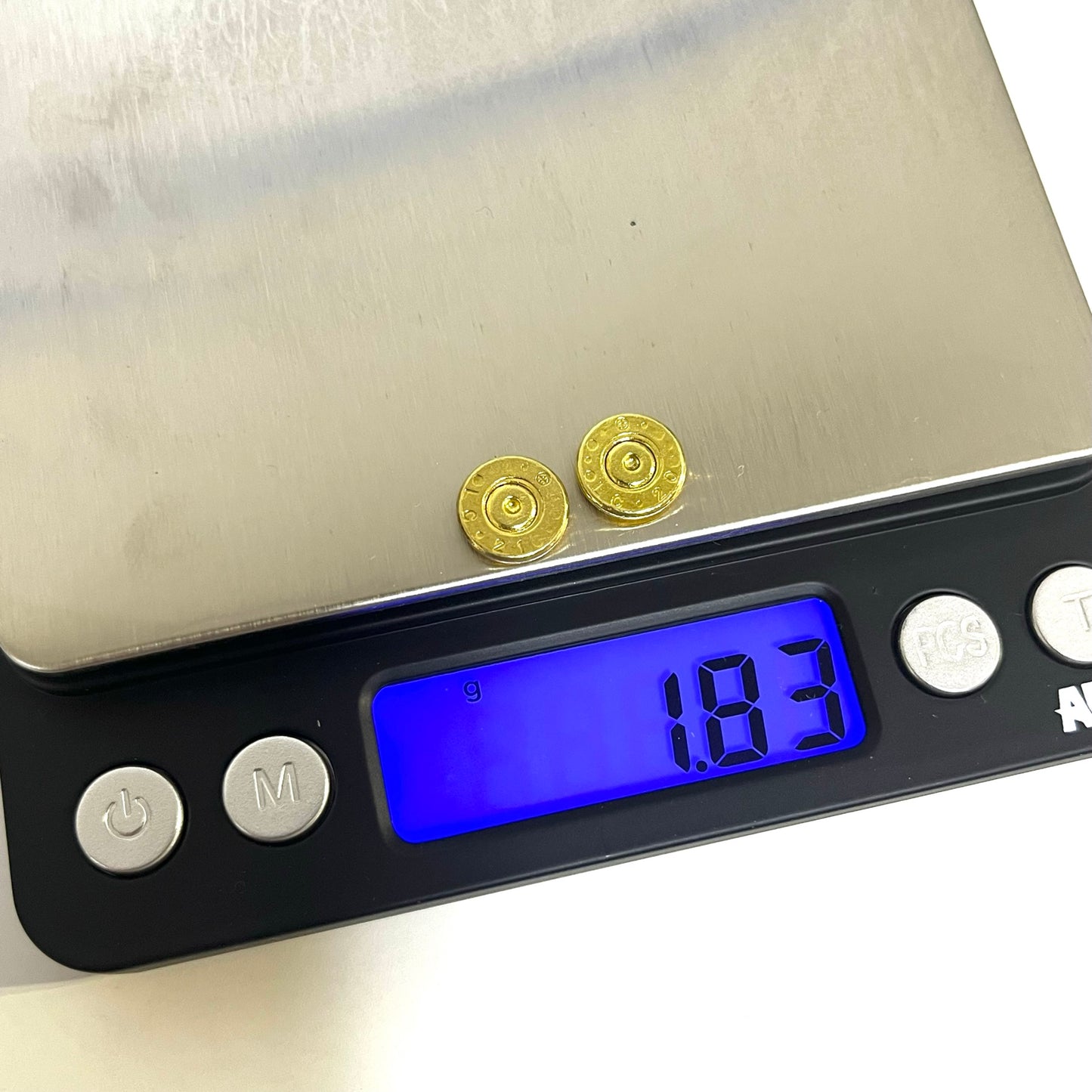 Upcycled 5.56 brass bullet casing slice being weighed for DIY stud earrings and metal crafts.