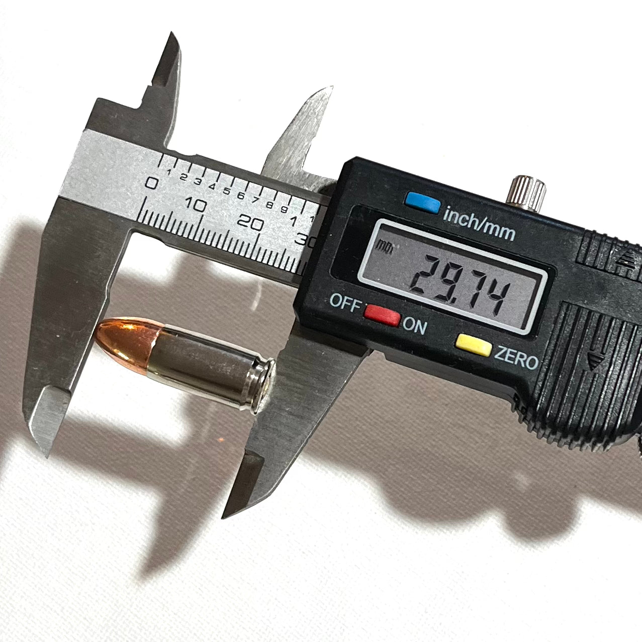 A digital caliper measuring the 29.74mm overall length of a 9mm nickel dummy round.