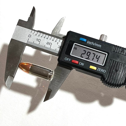 A digital caliper measuring the 29.74mm overall length of a 9mm nickel dummy round.