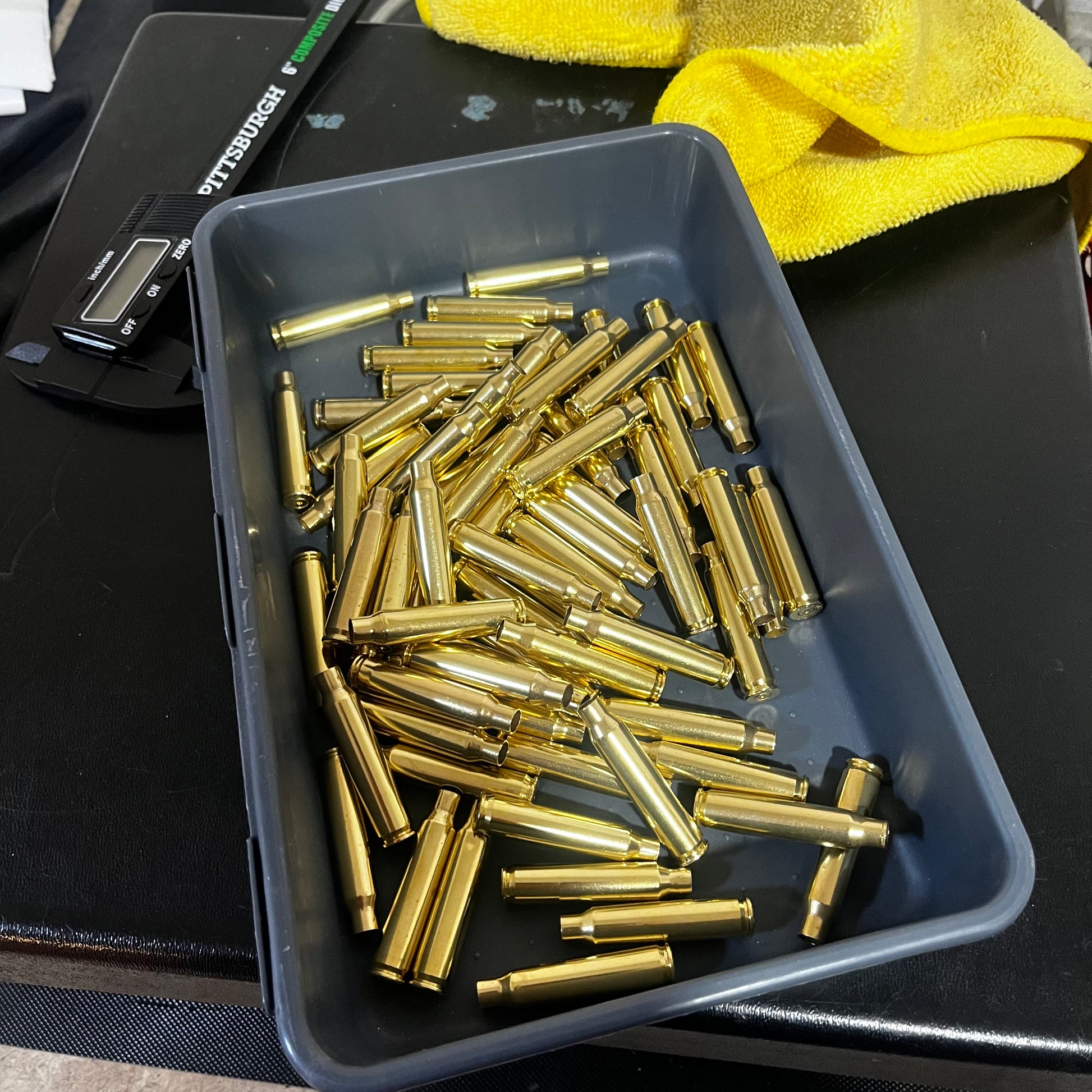Gray plastic tray filled with polished yellow .223 brass shells next to a black caliper and yellow cloth.
