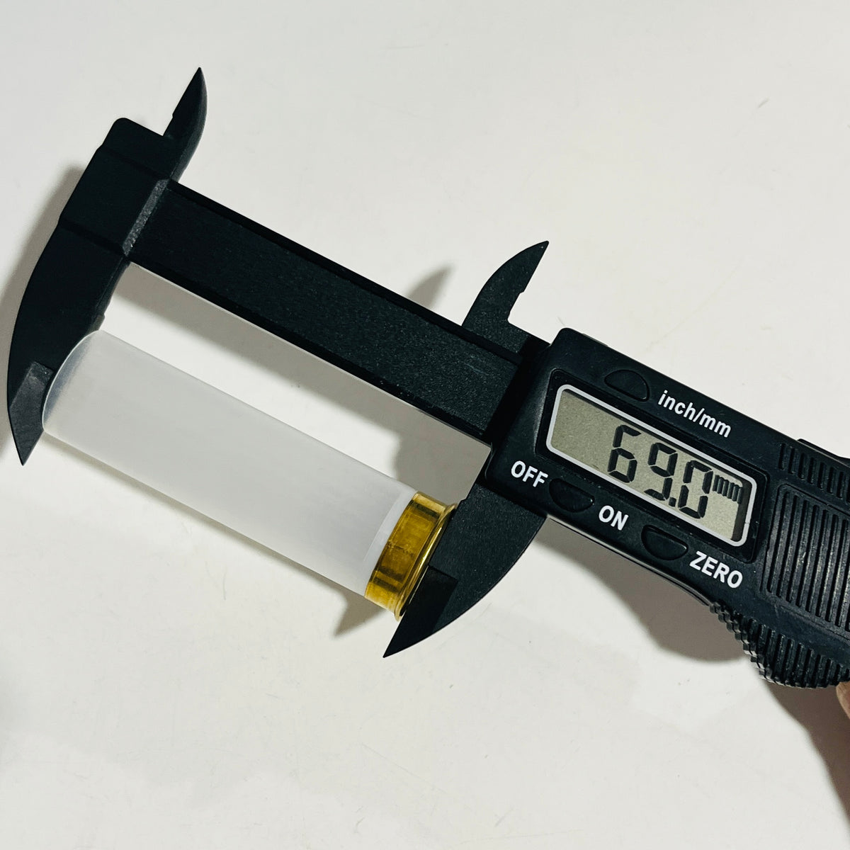 Digital caliper measuring the full length of a clear, empty 12 gauge hull at 69.0 mm