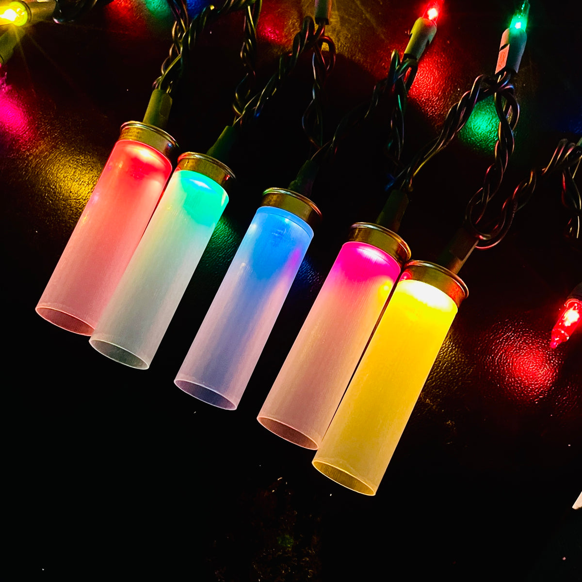 Five clear empty hulls fitted over Christmas mini lights, glowing red, green, blue, pink and yellow against a dark background